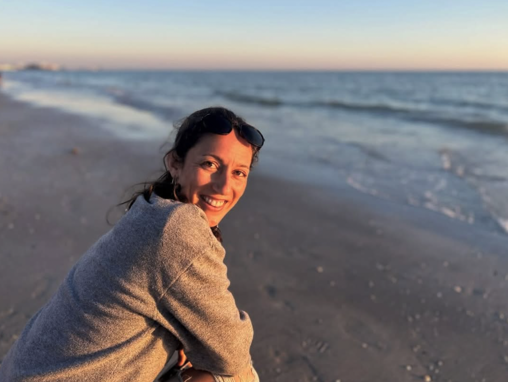 Studio founder sitting on a beach at sunset, smiling over her shoulder